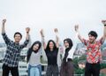 five young people hanging out and raise hand together on the building rooftop