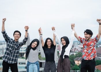 five young people hanging out and raise hand together on the building rooftop