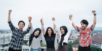 five young people hanging out and raise hand together on the building rooftop